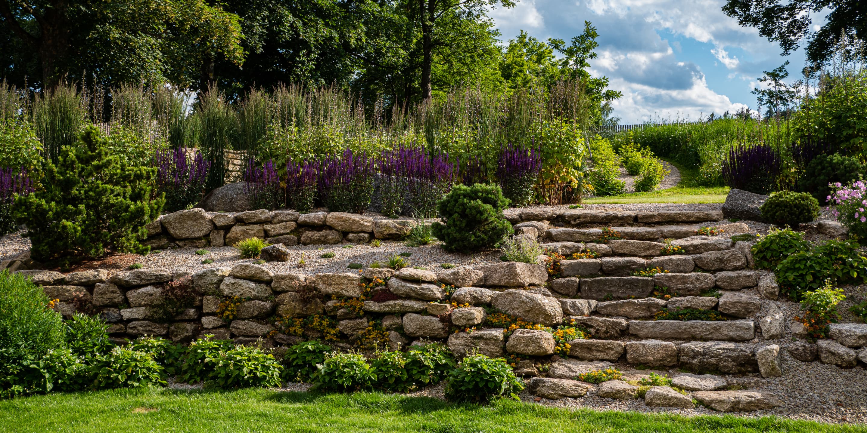 Přírodní zahrada bez chemie s rozkvetlou loukou a kamennými schody