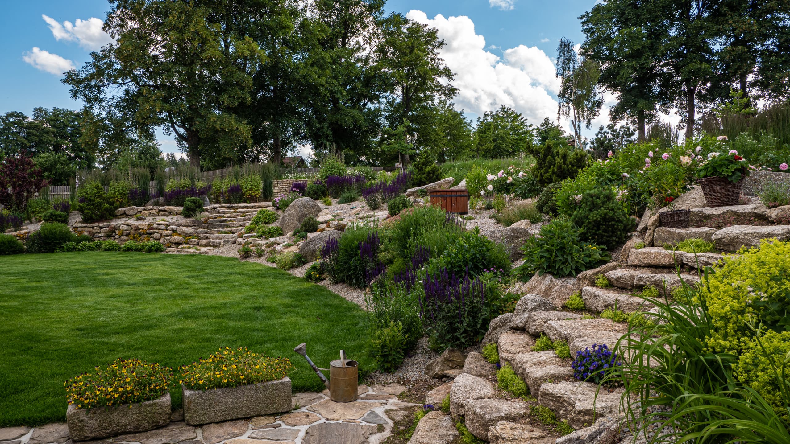 alt="Ekologická zahrada s trávníkem, kameny a vodním prvkem v přírodním stylu"