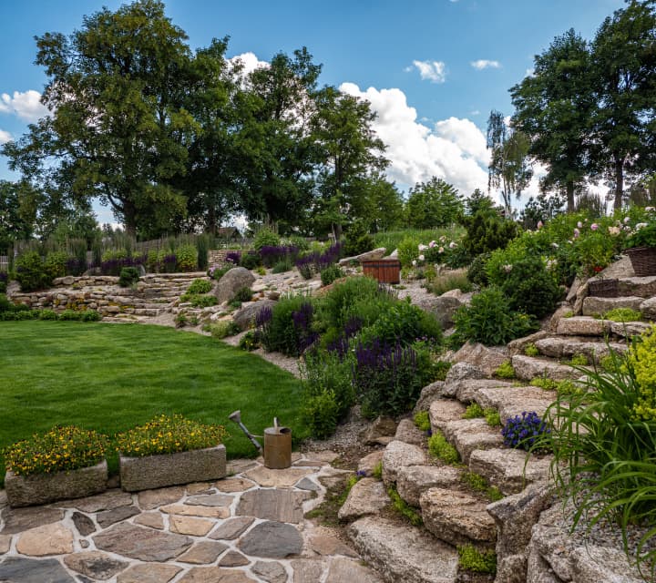 alt="Ekologická zahrada s trávníkem, kameny a vodním prvkem v přírodním stylu"